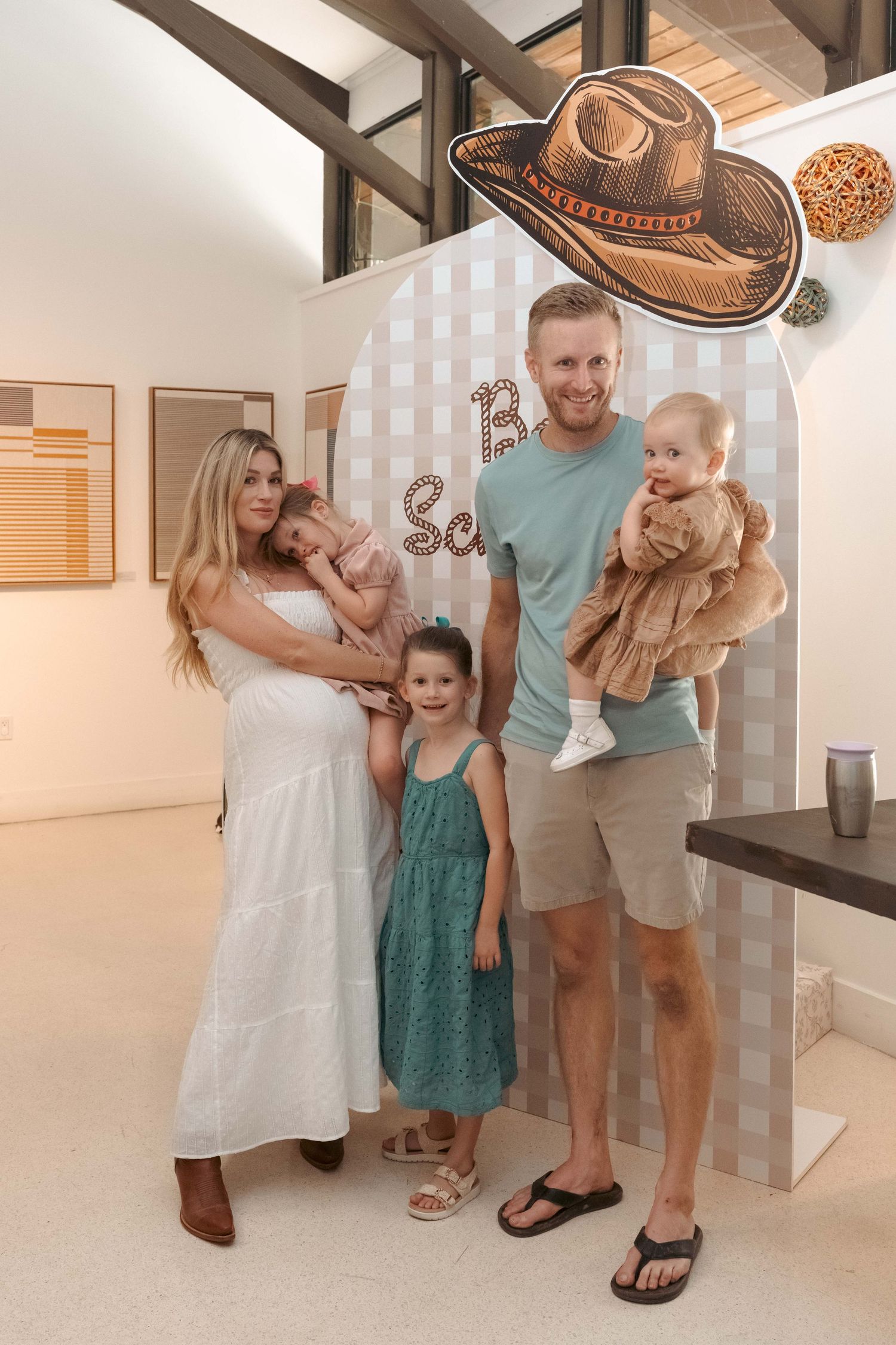 Smiling family with two young daughters poses together at a western-themed baby shower photo backdrop.