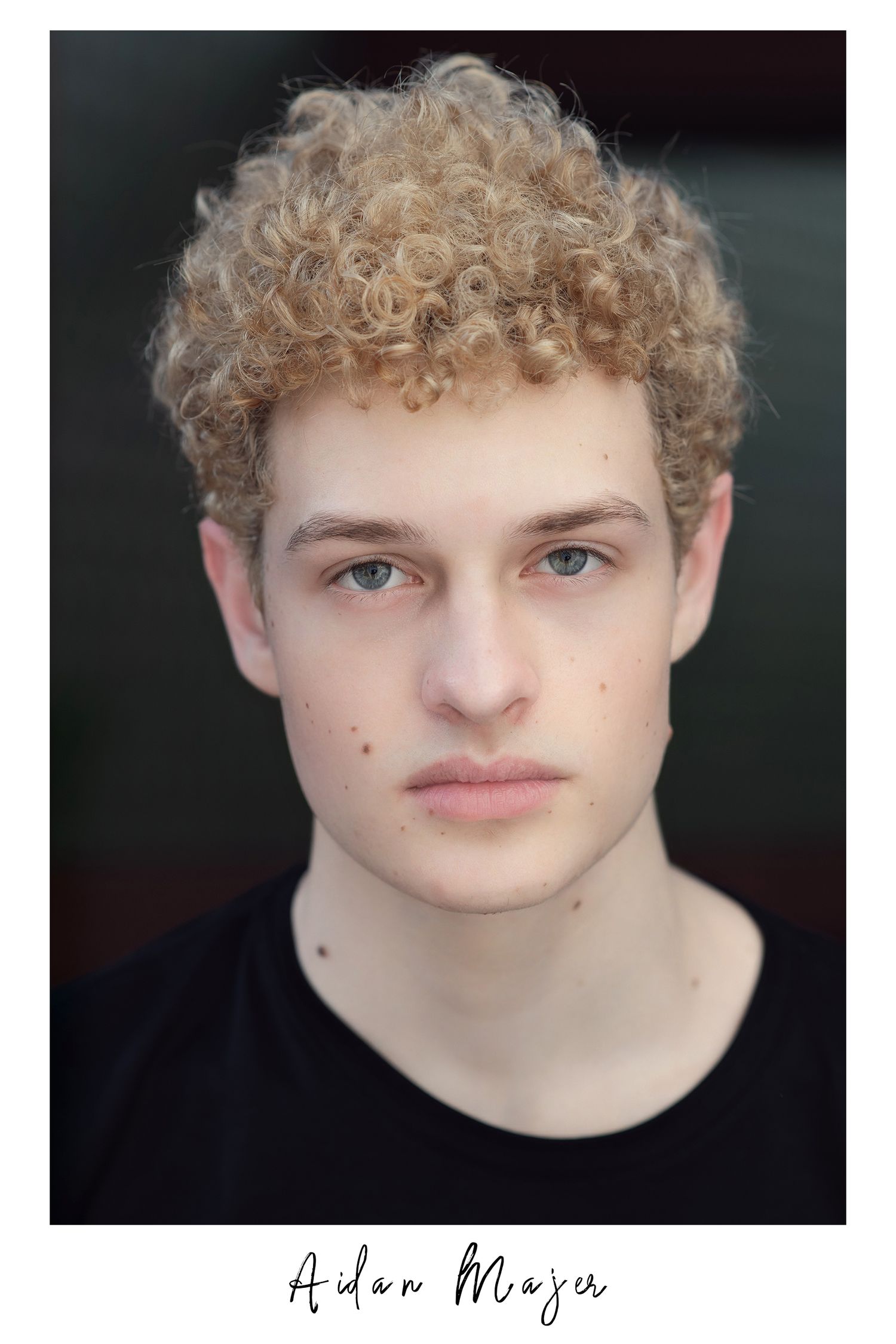 Professional headshot of young male model Aidan Majer with curly blonde hair and blue eyes.