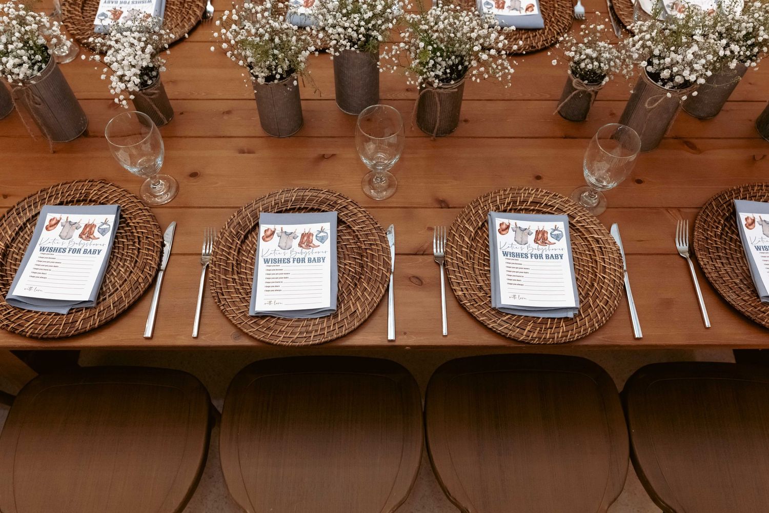 Elegant rustic wooden dining table set with wicker charger plates, glassware, and baby's breath centerpieces.