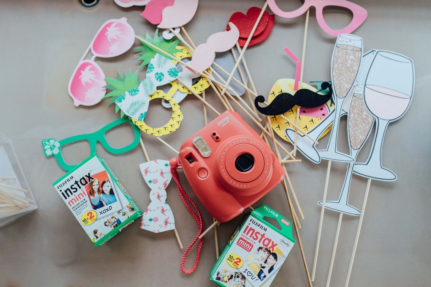 Fujifilm Instax Mini camera with colorful photo booth props and film packs on a white surface.