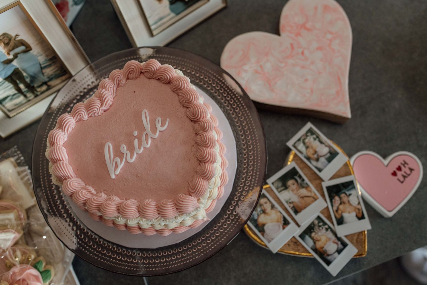Pink heart-shaped bride cake displayed with Polaroid photos and heart decorations on a table.