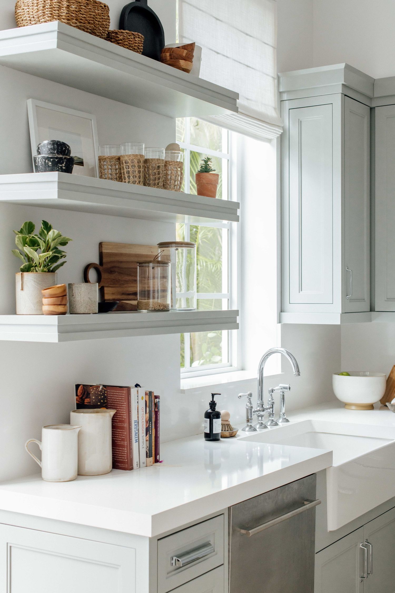 Light gray kitchen with open shelving, white quartz countertops, and bridge faucet over farmhouse sink.