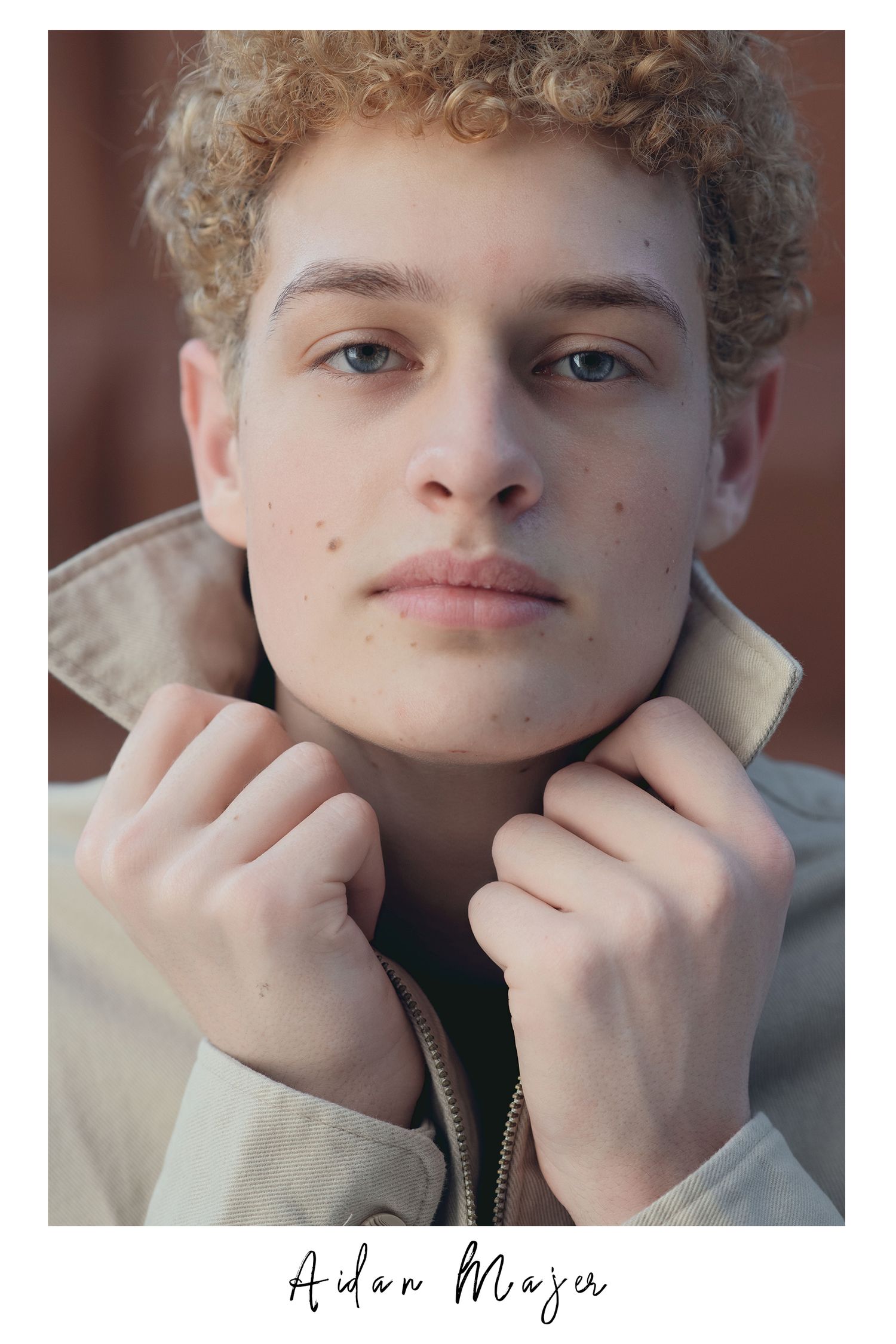 Close-up portrait of young man with curly hair holding jacket collar, modeling headshot.