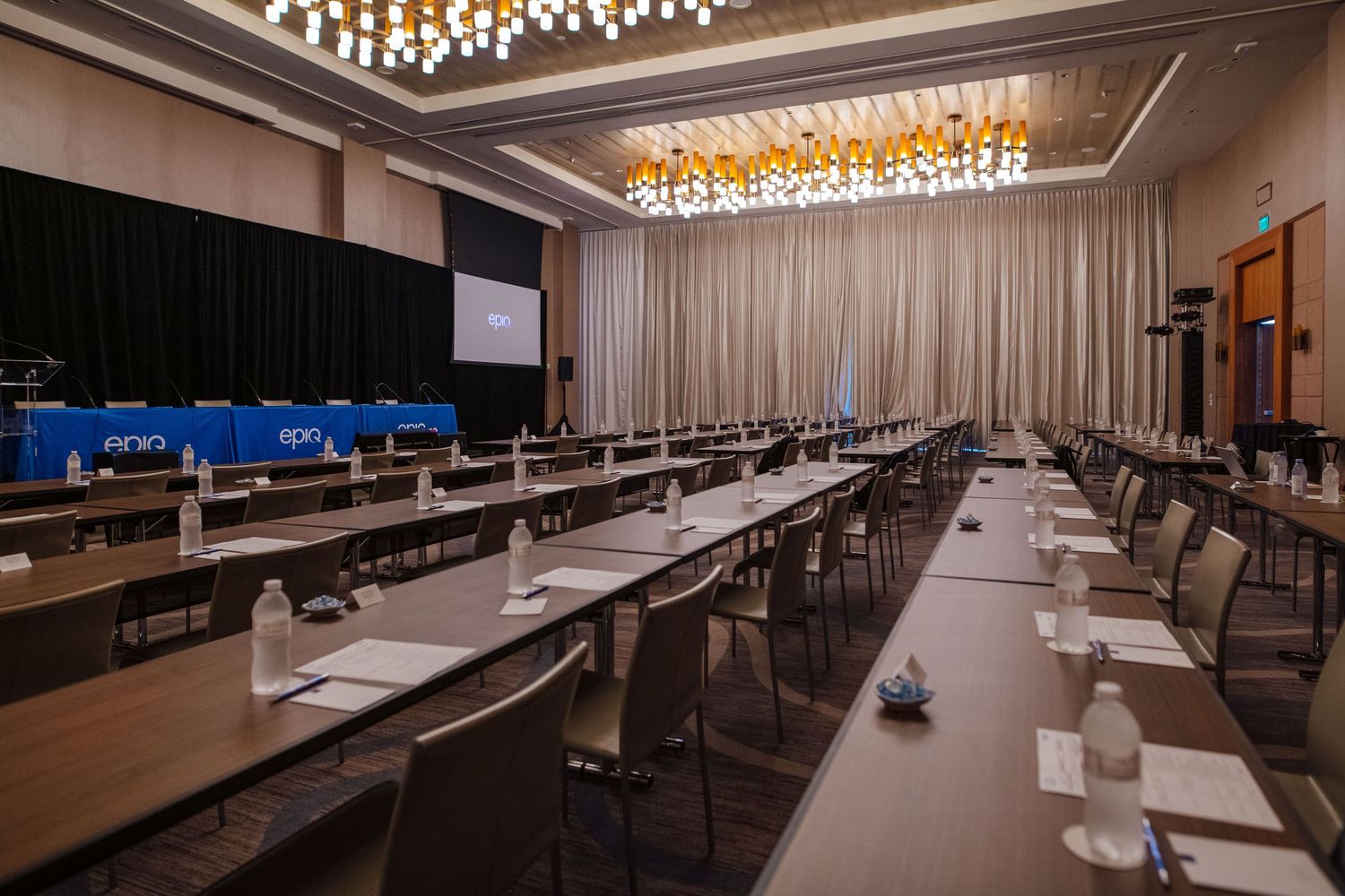 Large conference room with classroom-style seating, projection screen, and elegant chandelier lighting.