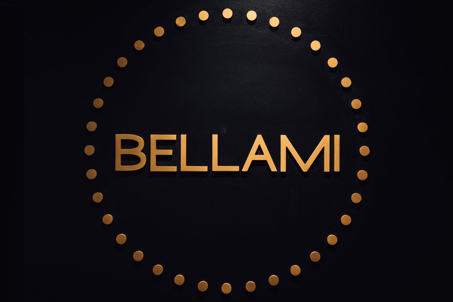 BELLAMI gold logo on black background with circular dotted border, luxury hair brand signage.