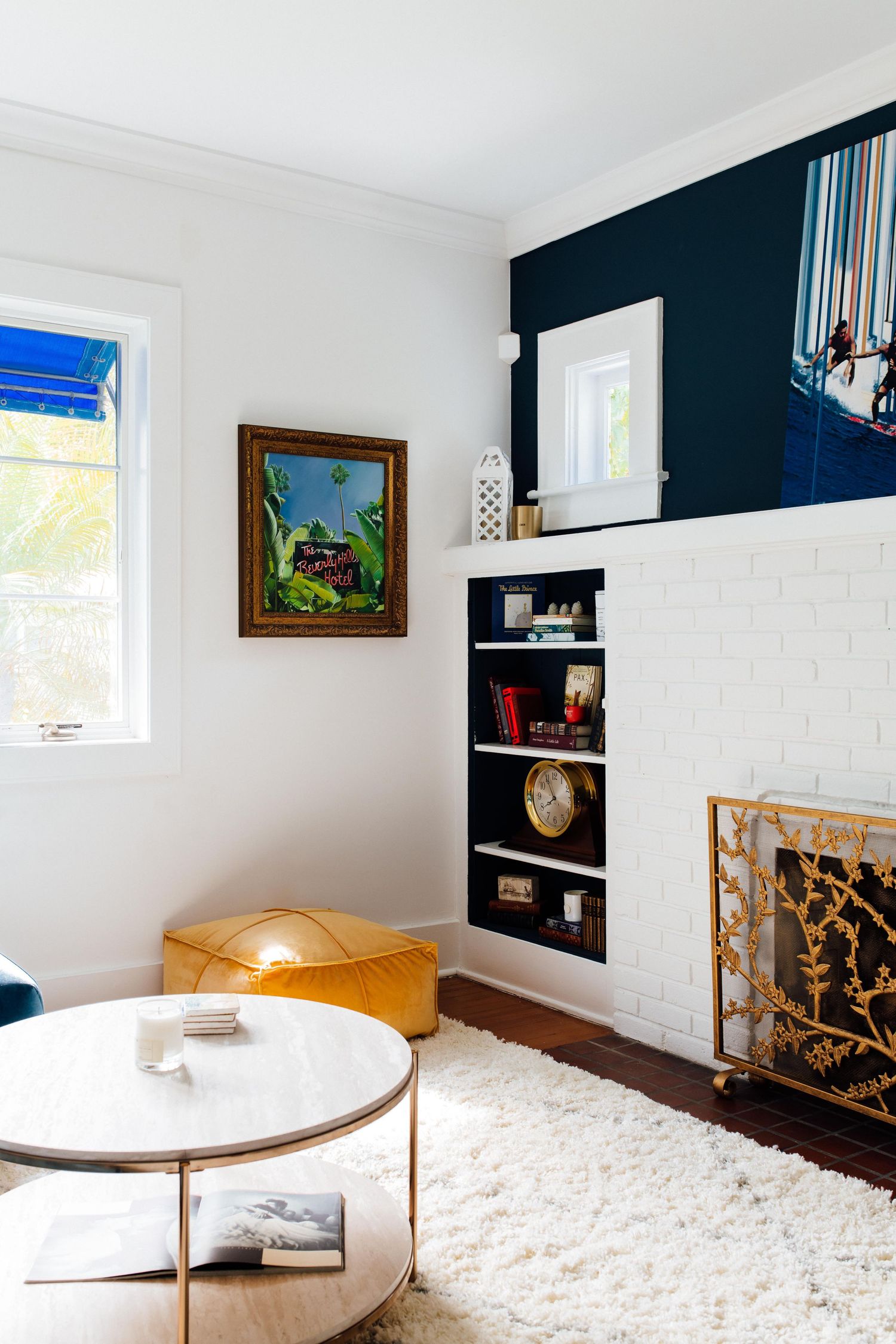 Cozy living room with white brick fireplace, built-in shelves, shag rug, marble coffee table, and navy accent wall.