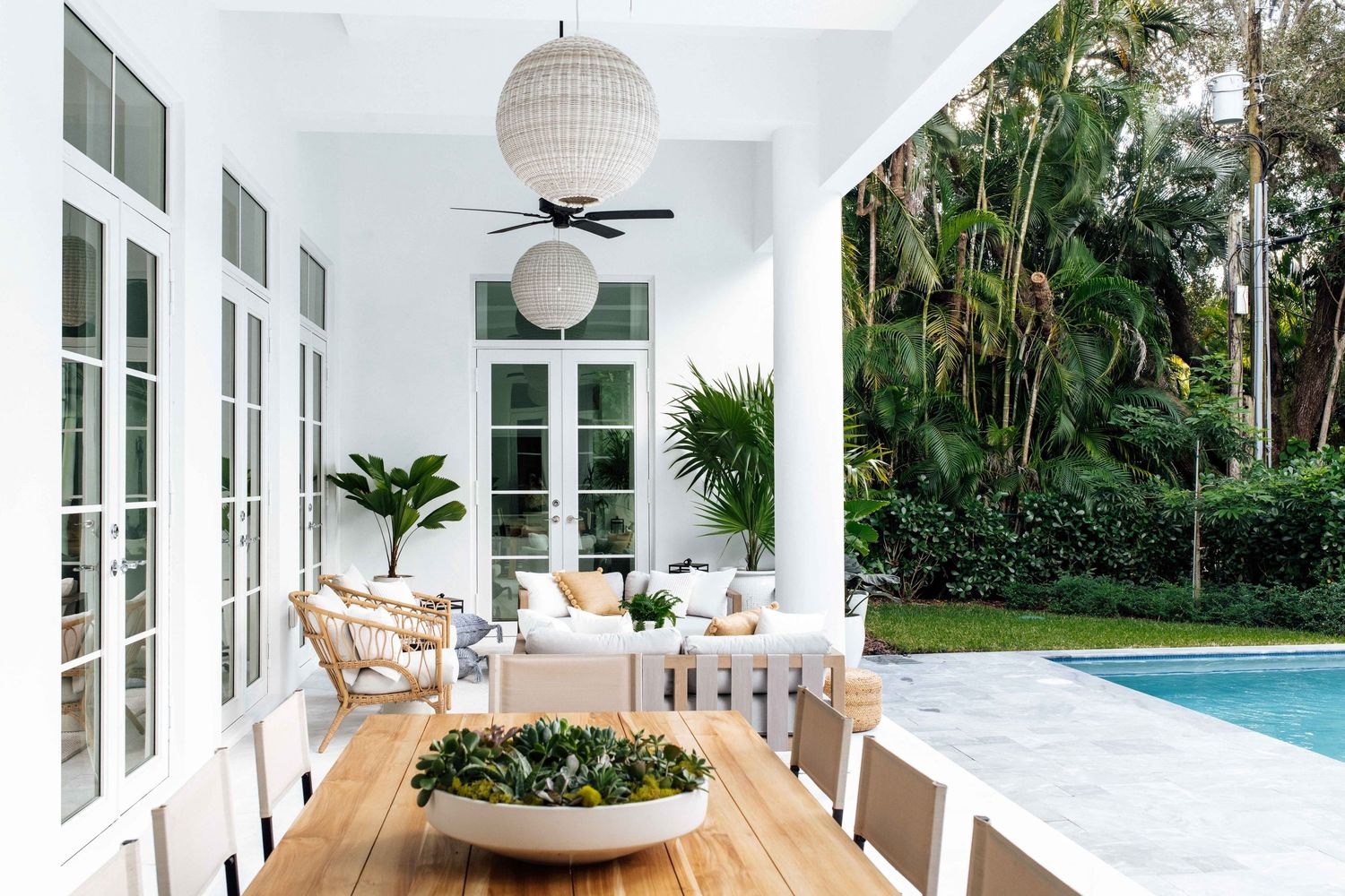 Bright white covered patio with outdoor dining, seating, and lush tropical garden by pool.