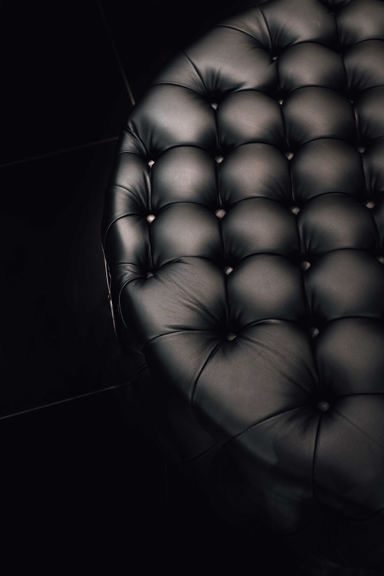 Close-up of luxurious black tufted leather upholstery with button details on a curved sofa.
