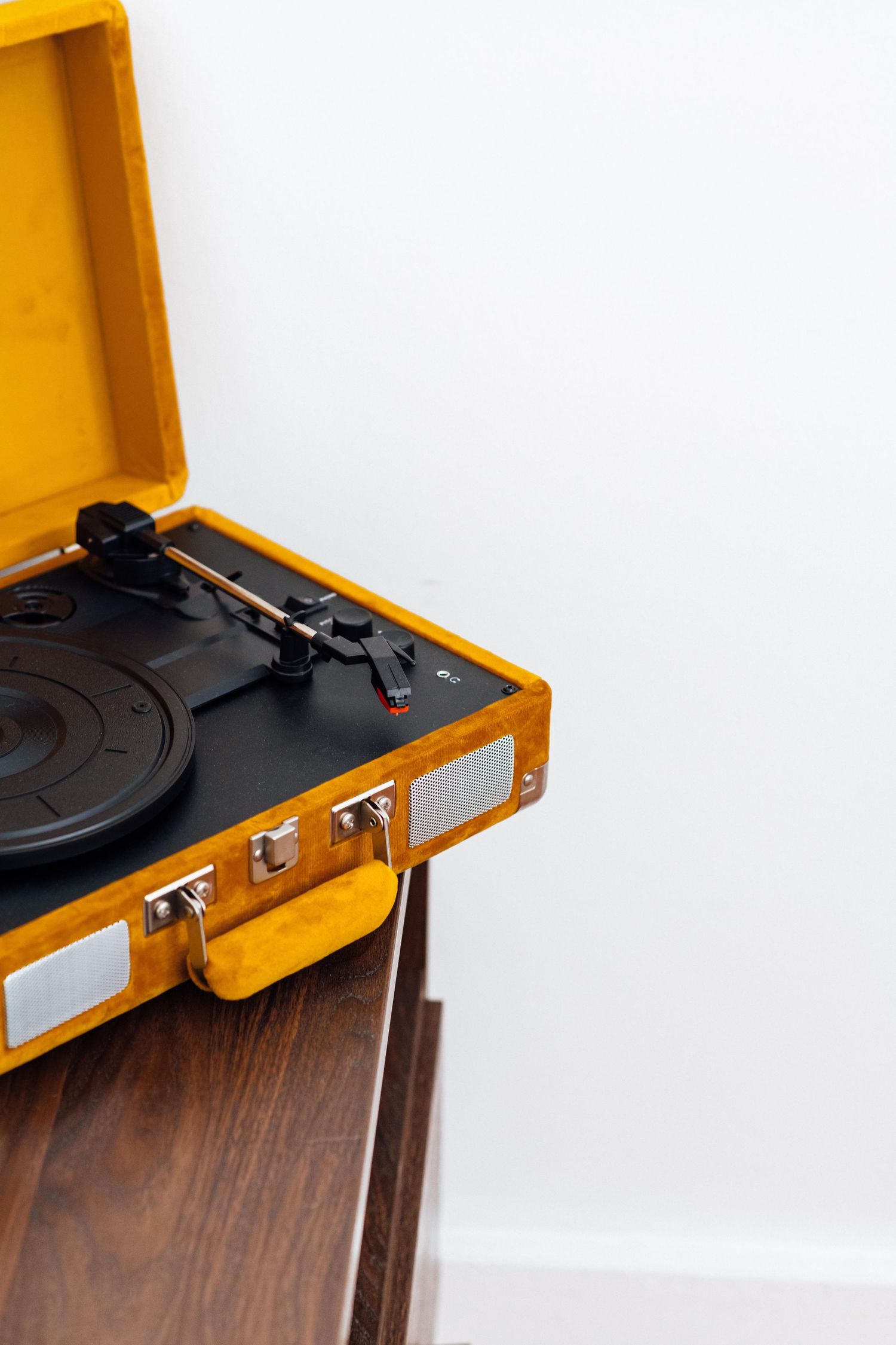 Vintage yellow portable record player turntable open on a wooden cabinet against a white wall.