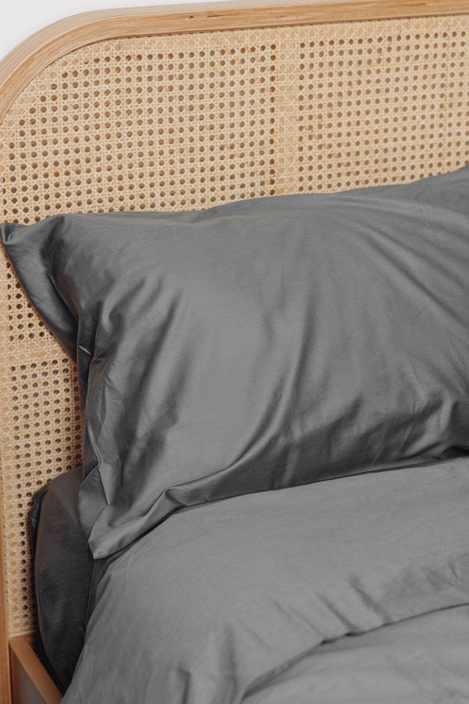 Gray pillow and bedding on a rattan headboard bed in a cozy bedroom.