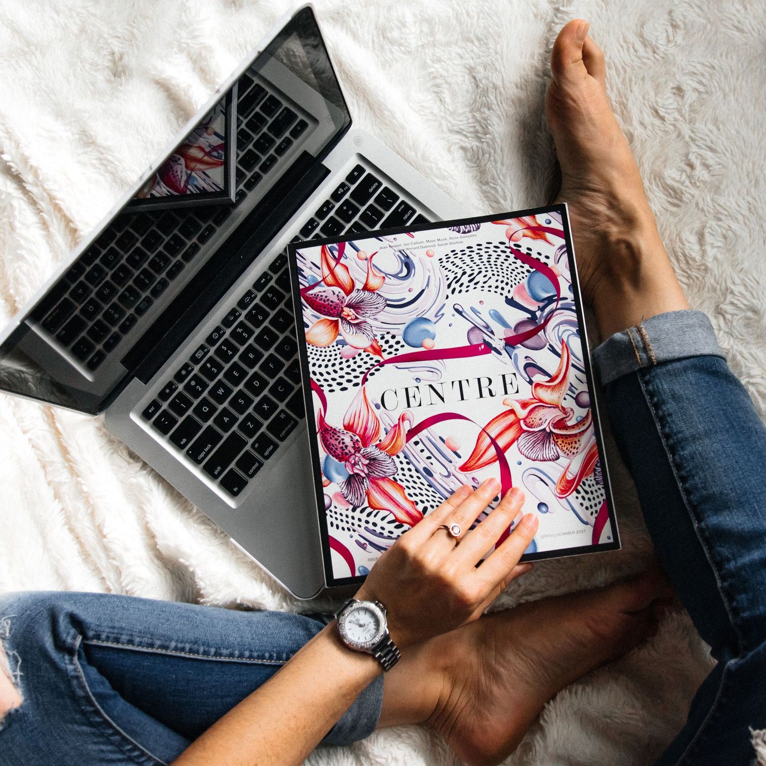 Person relaxing with laptop and Centre magazine on white fur blanket.