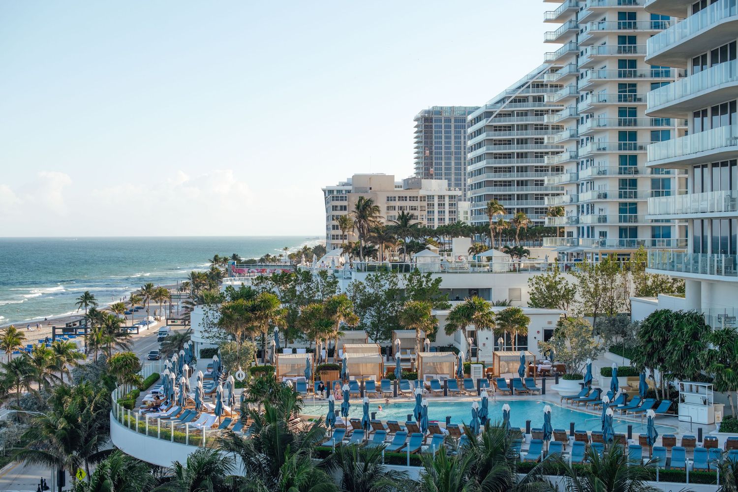 Aerial view of beachfront luxury hotel with large pool, palm trees, and ocean coastline in Florida.