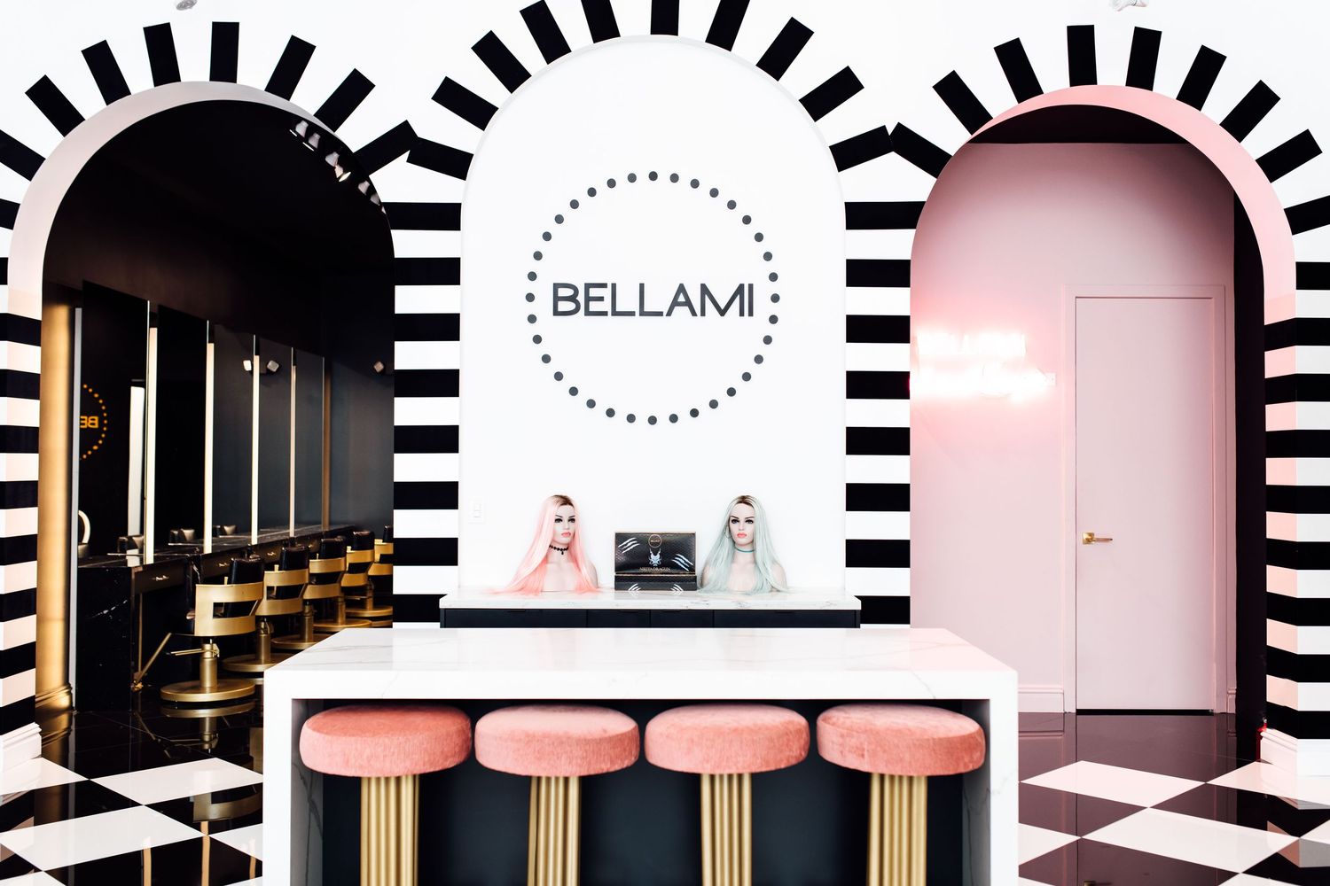 Bellami salon reception desk with pink stools, striped arches, checkered floors, and two receptionists in a stylish interior.