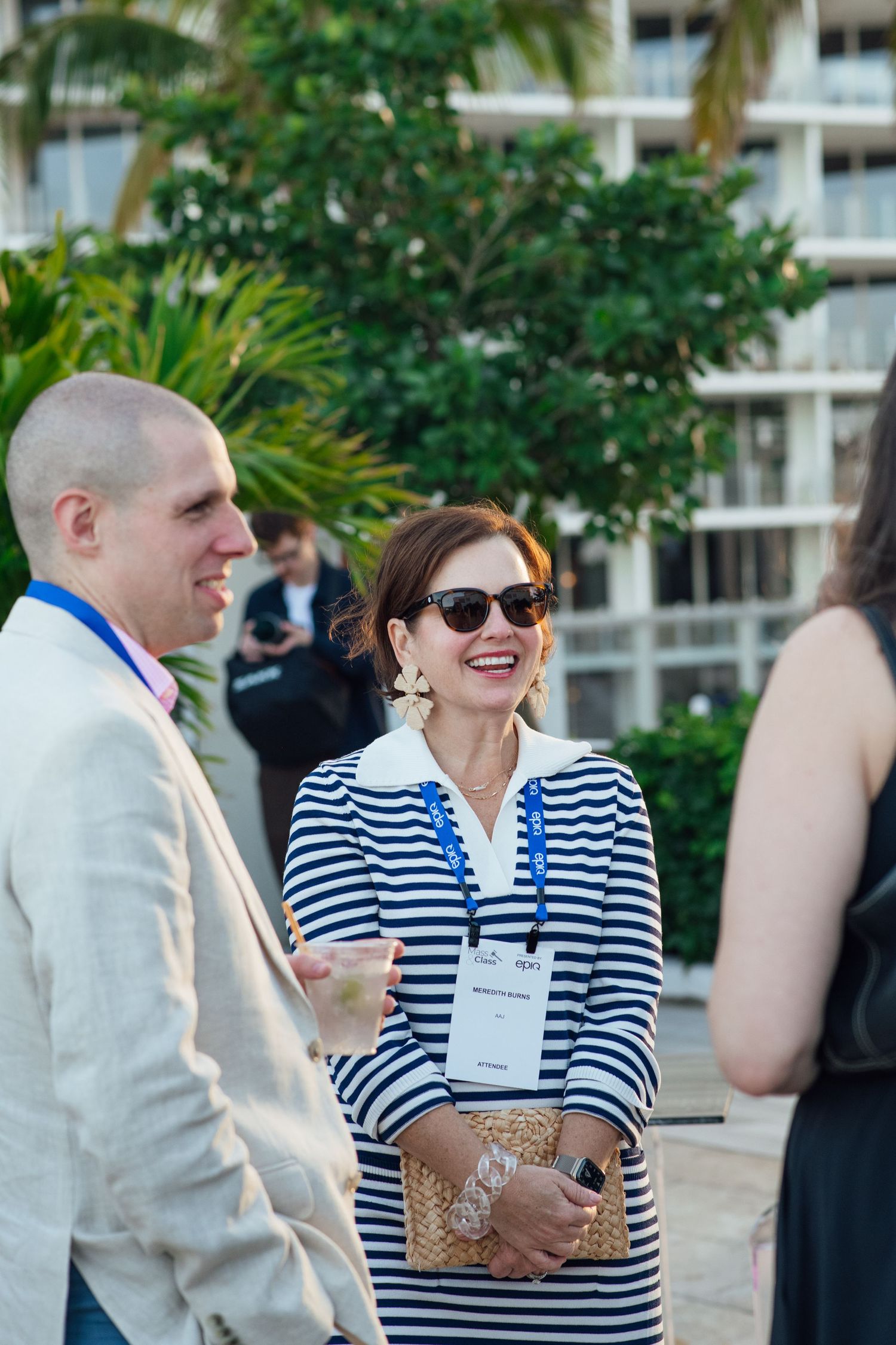 Professional woman in striped dress with conference badge laughing at outdoor corporate networking event.