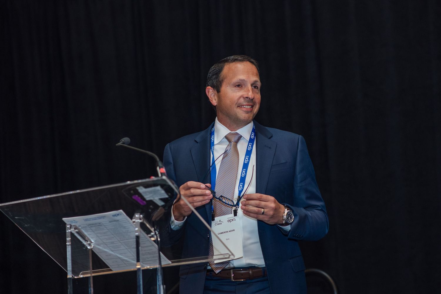Business professional in blue suit speaking at podium during corporate conference presentation.