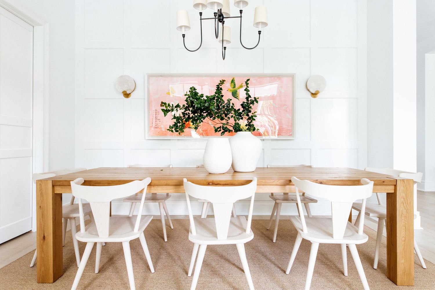Elegant white dining room with wood table, white chairs, chandelier, and pink botanical artwork.