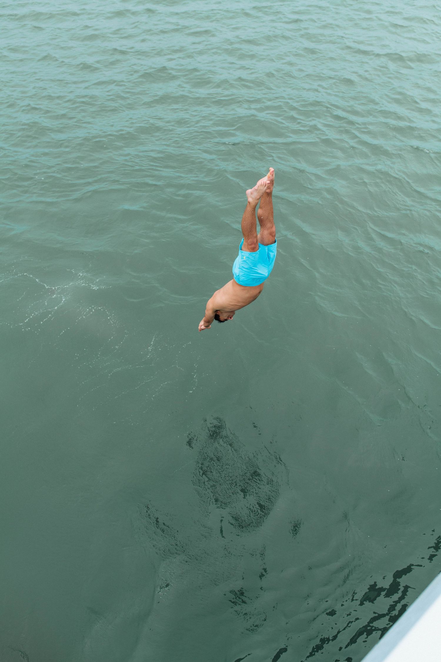 Person in blue swimsuit diving headfirst into calm turquoise ocean water from a boat.