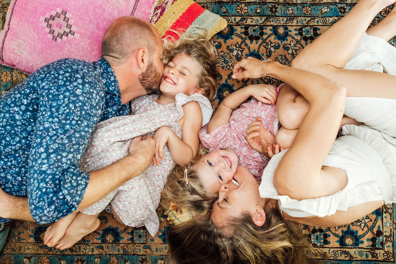 Aerial view of happy family with two young children relaxing together on a vibrant patterned rug.