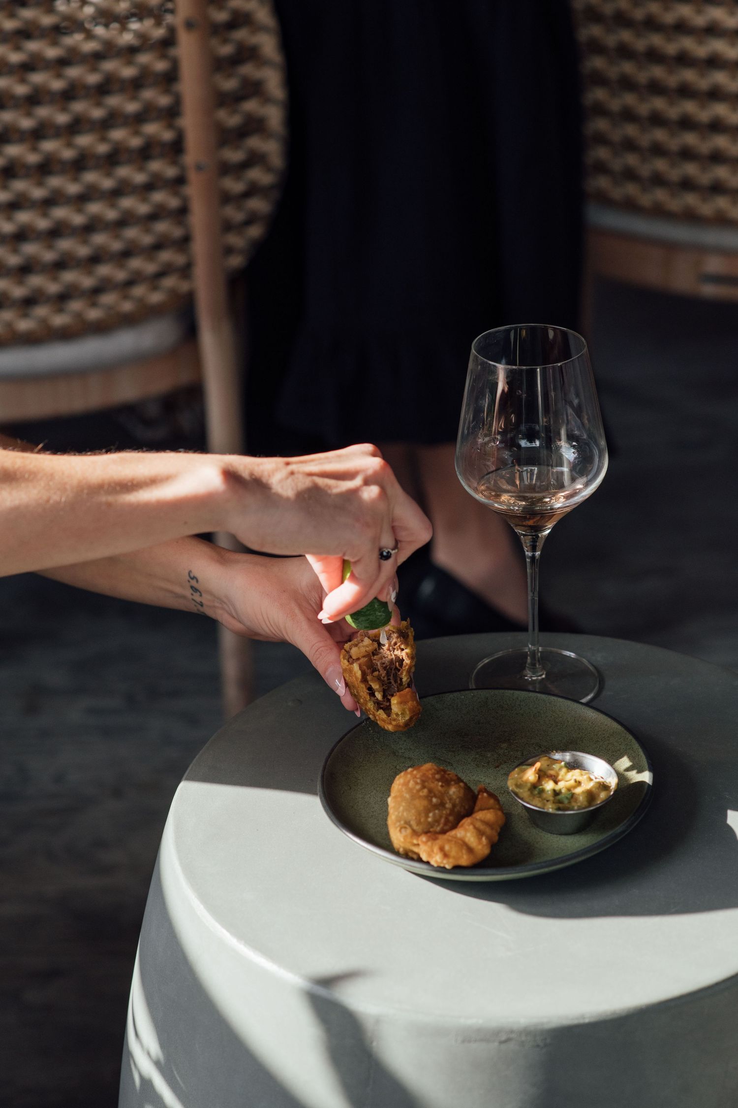 Hand picking up a gourmet appetizer from a dark plate beside an empty wine glass outdoors.