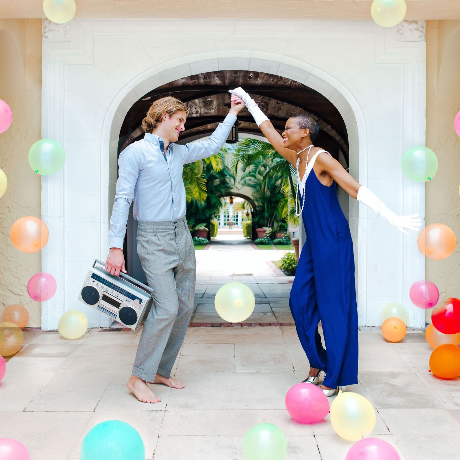Joyful interracial couple dancing with colorful balloons and a boombox at an outdoor celebration.