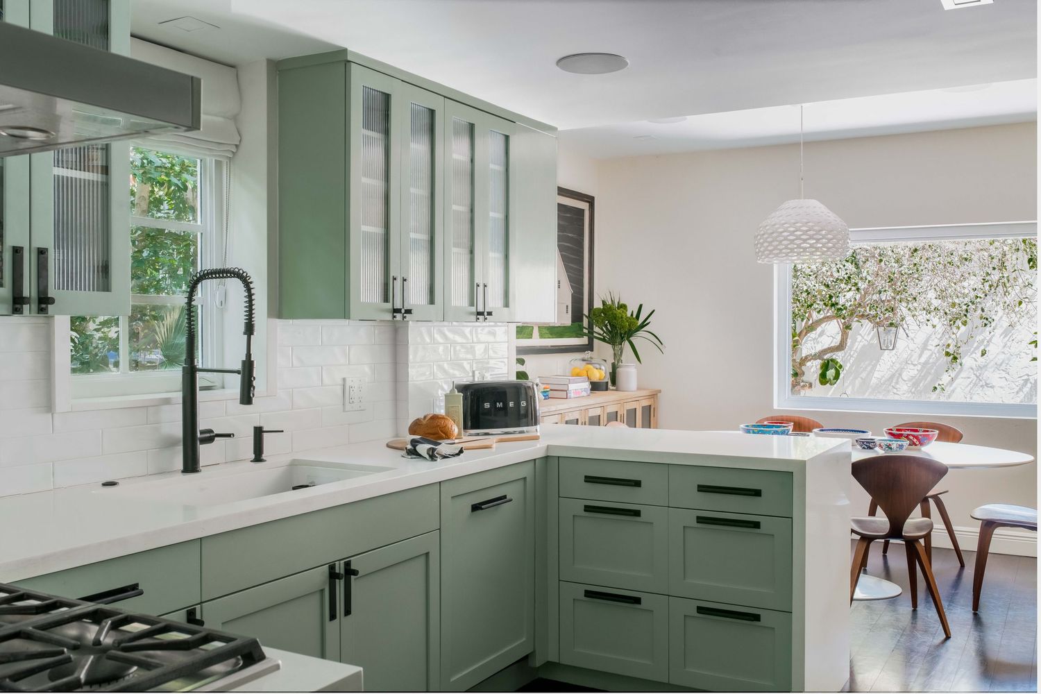 Modern kitchen with sage green cabinets, white quartz countertops, black hardware, subway tile backsplash, and natural light.