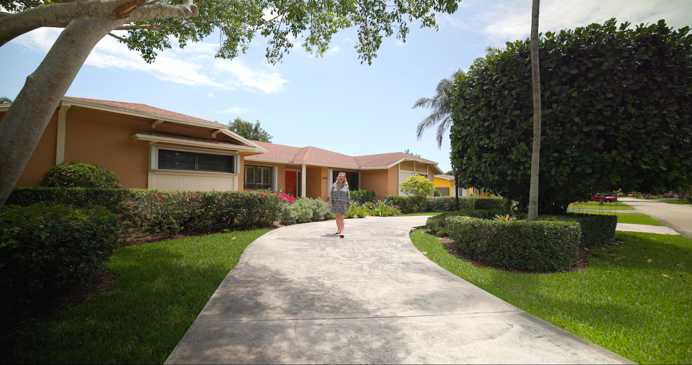 Curving concrete walkway leading to peach-colored residential buildings with tropical landscaping.