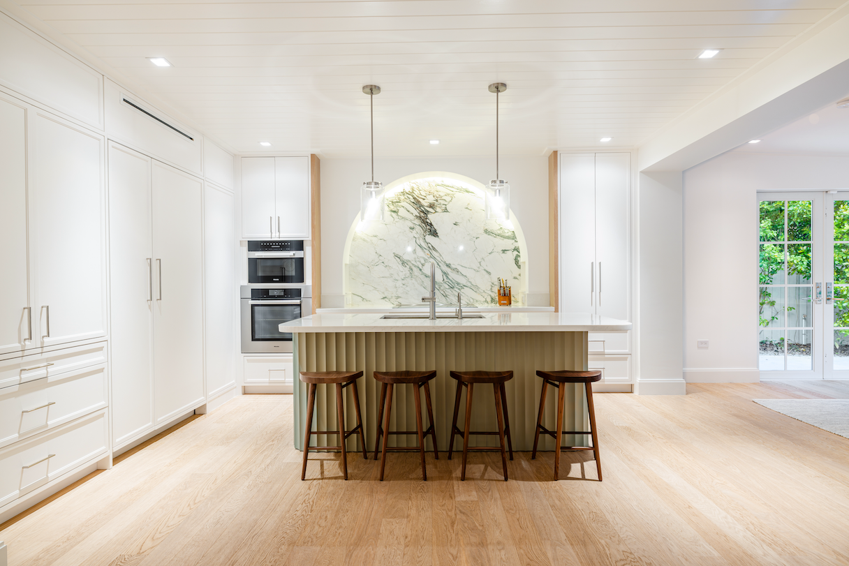 Modern white kitchen with light wood floors features a floating island, black bar stools, and a dramatic round marble backsplash.