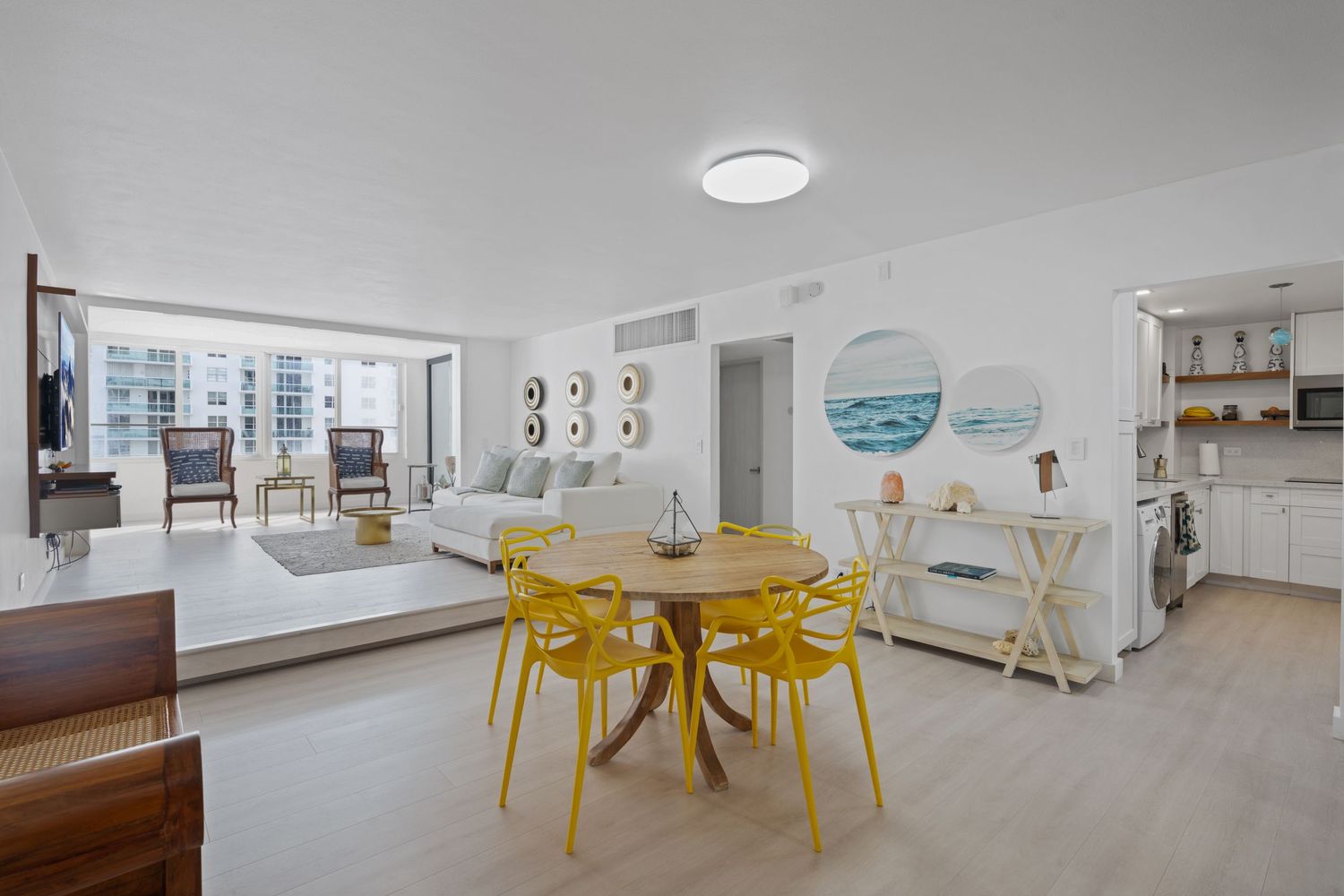 Modern apartment interior with bright yellow dining chairs, wood floors, and white walls showcasing ocean-themed wall art.
