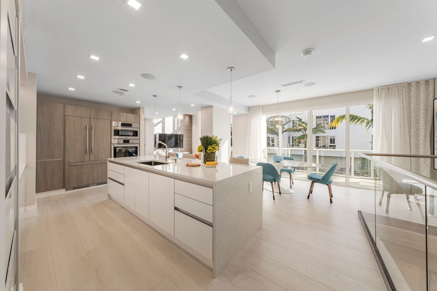 Modern bright open concept kitchen with white island, light wood floors, and turquoise dining chairs in contemporary home.