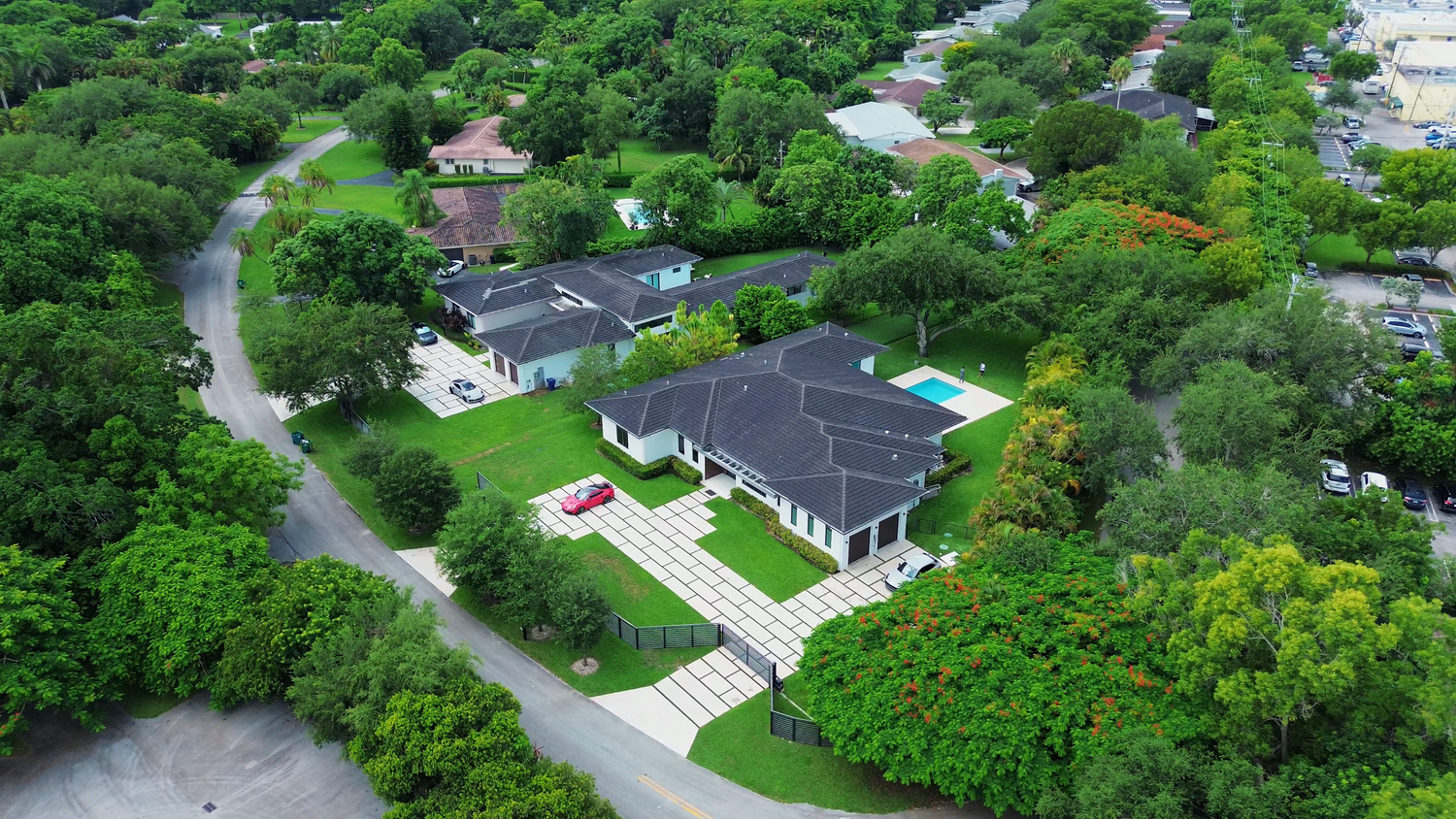 Aerial view of a modern grey house with white trim surrounded by lush green trees and curved driveway.
