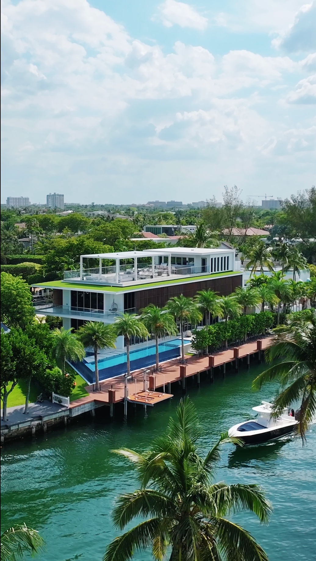 Modern luxury waterfront home with rooftop terrace and swimming pool along canal with boat dock in tropical setting.