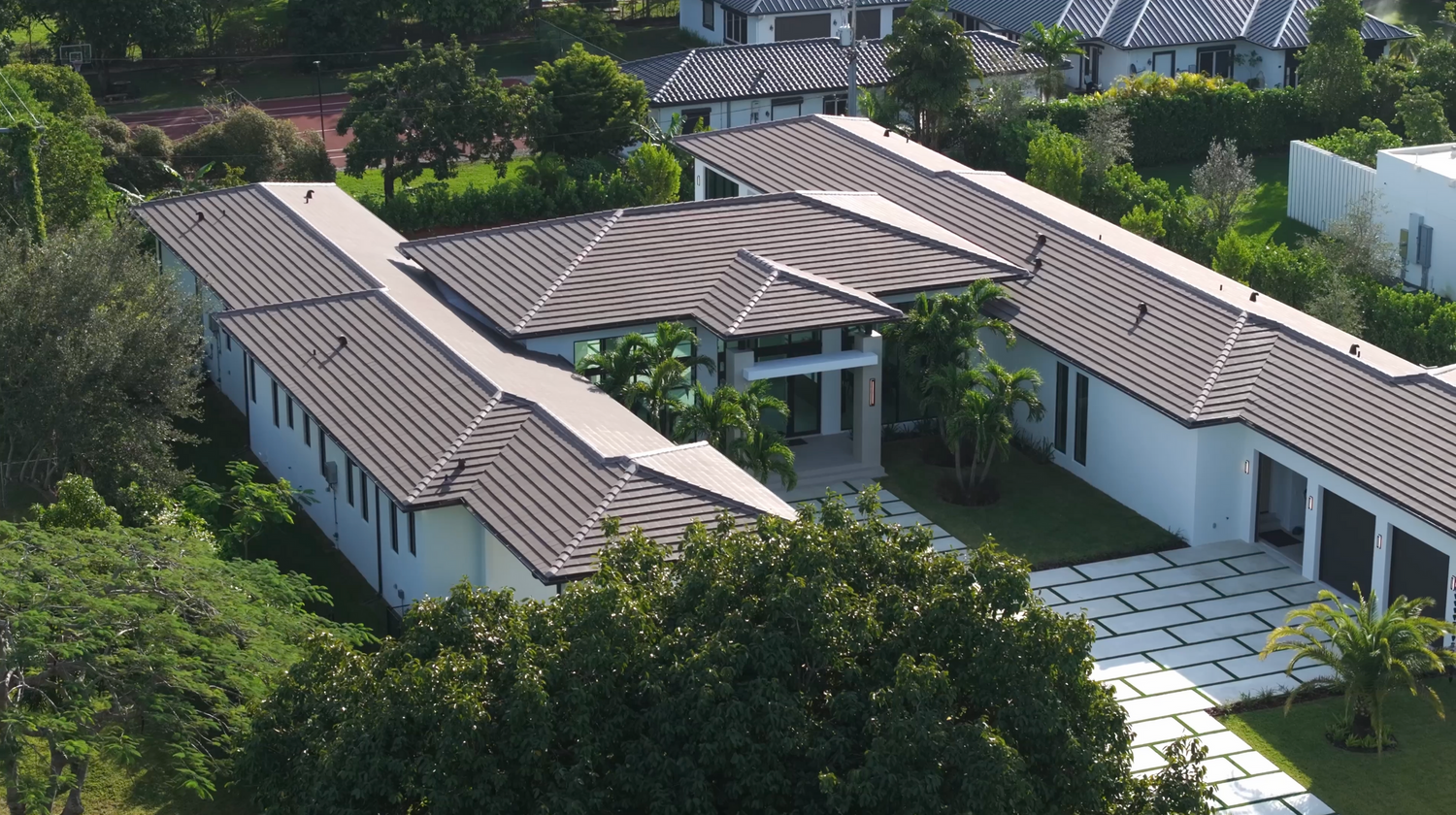 Aerial view of a luxurious white contemporary villa with terracotta roofs and a courtyard surrounded by lush greenery.
