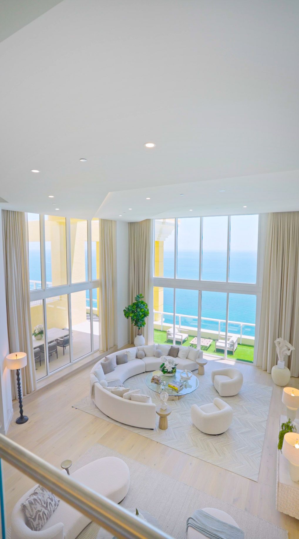 Luxurious penthouse living room with curved white sofa and stunning ocean views through floor-to-ceiling windows.
