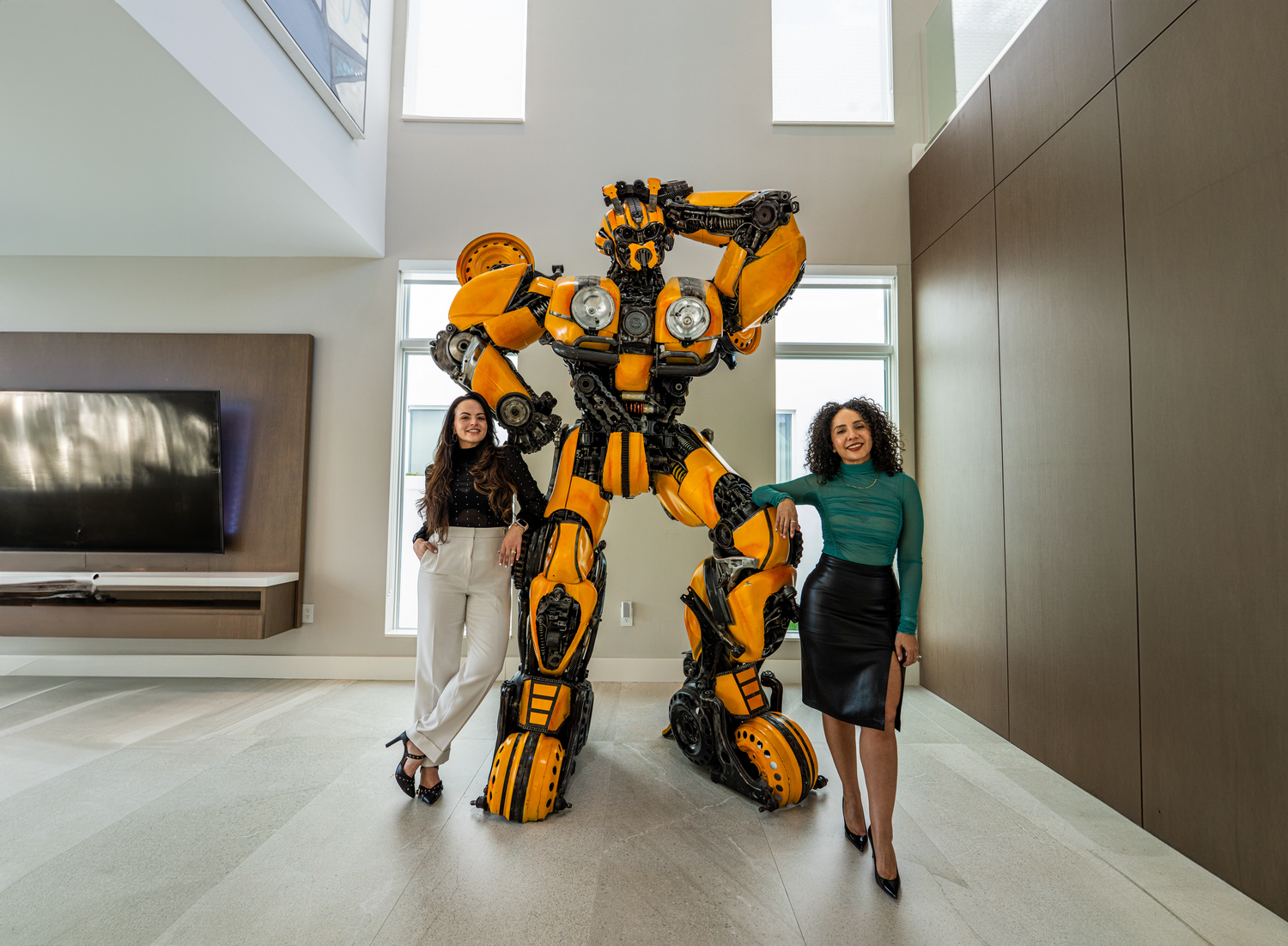 A tall yellow and black Bumblebee Transformer costume stands in a modern living room with high ceilings.