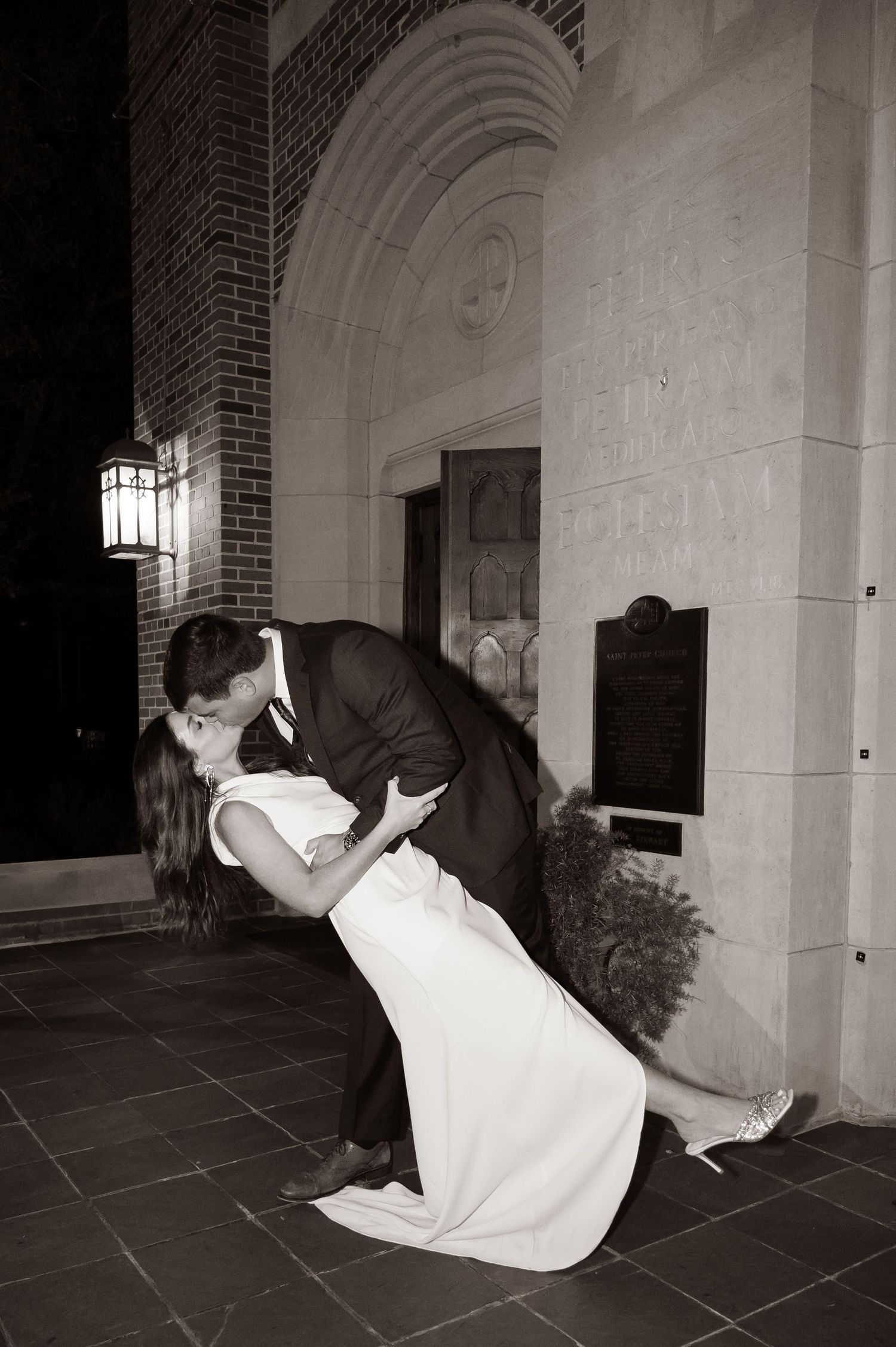 Romantic couple shares a dramatic dip kiss under an arched entryway in black and white photography.
