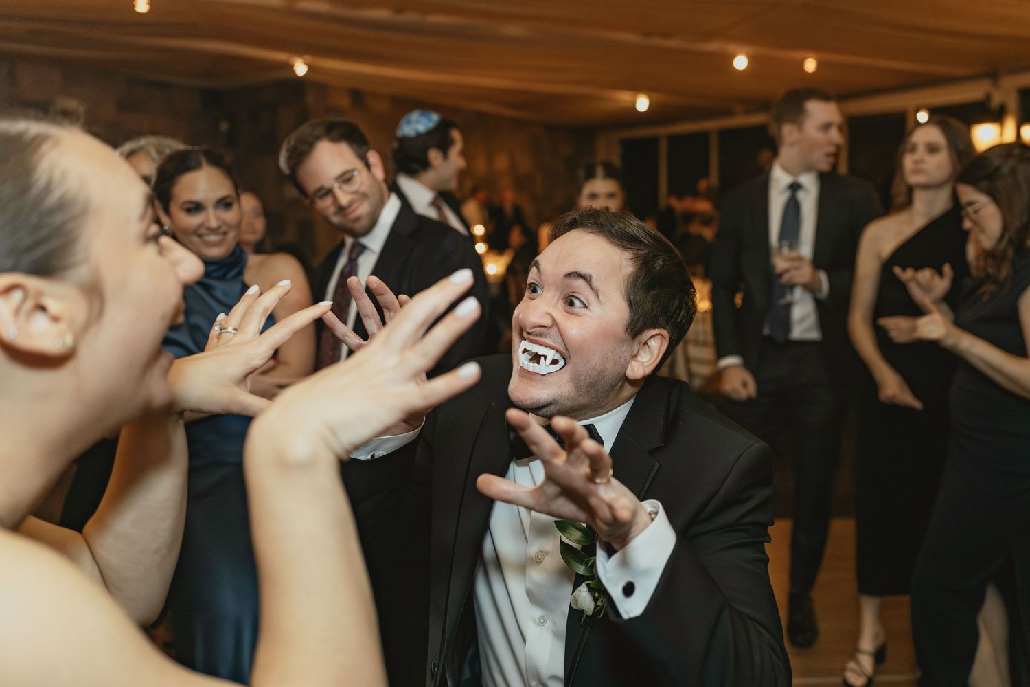 Wedding guests dance and celebrate joyfully on a dimly lit dance floor at an indoor reception.