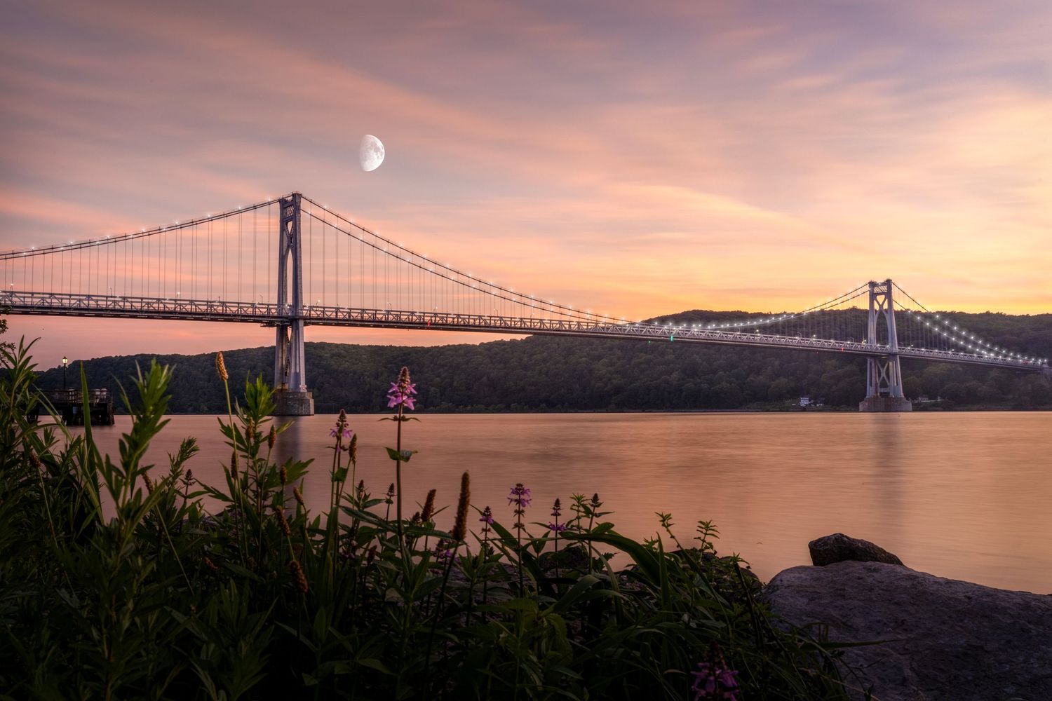 A stunning sunset panorama of the San Francisco Bay Bridge with the moon rising in a pink and orange sky.