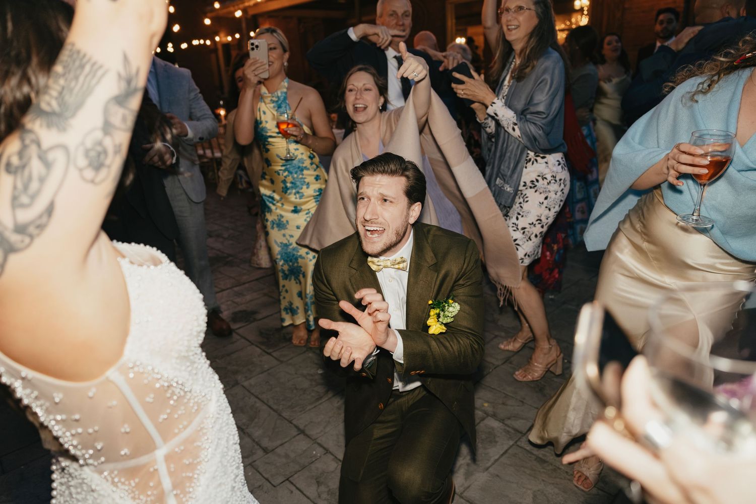 Wedding reception guests dancing and celebrating under twinkling lights at dusk.