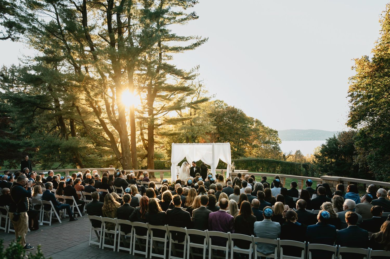 Outdoor wedding ceremony setup with white chairs facing a scenic ocean view during golden hour sunset.