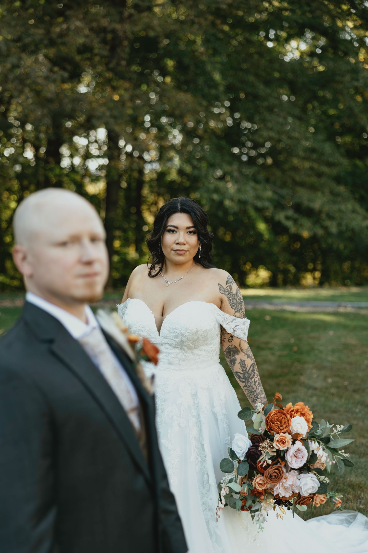 Wedding couple poses outdoors with autumn-inspired floral bouquet featuring burnt orange and blush roses in a garden setting.