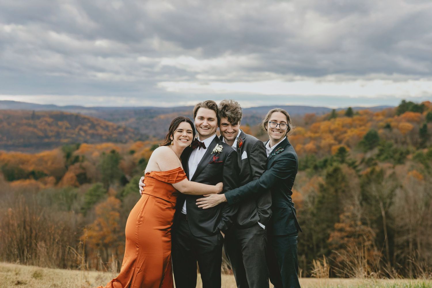 Wedding party poses together on a scenic hilltop during autumn with colorful fall foliage in the background.