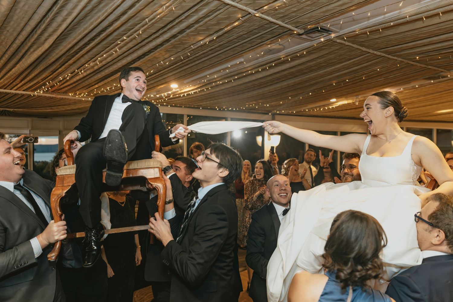 Wedding reception celebration under a tent with string lights and dancing guests.