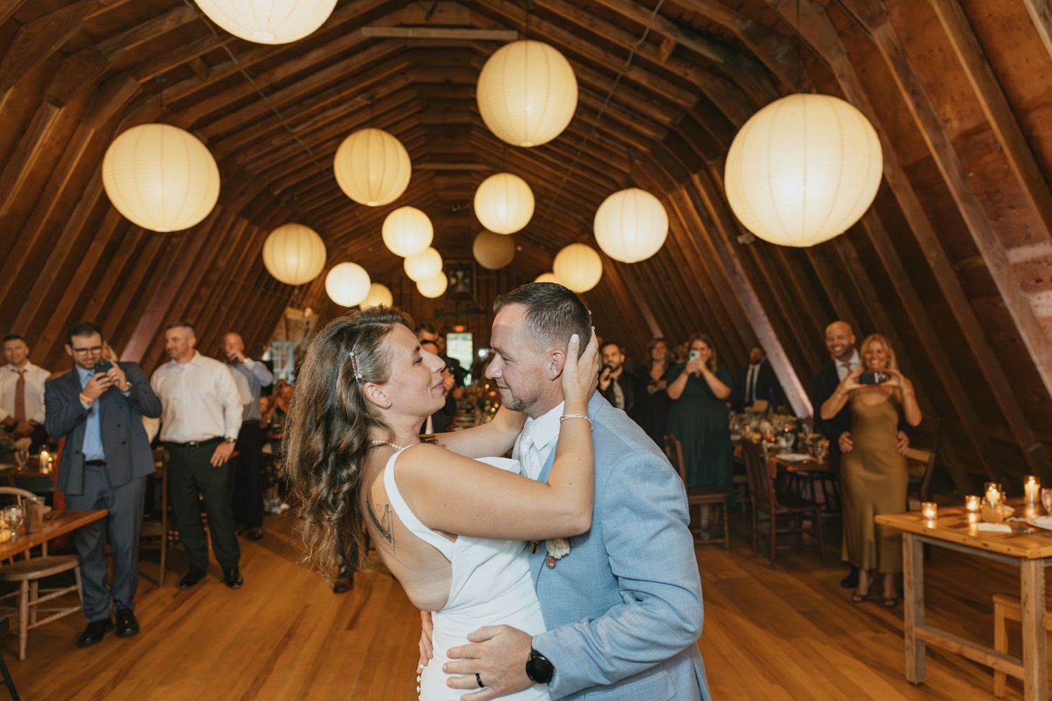 Couples dance together in a rustic barn venue decorated with glowing paper lanterns during a wedding reception.