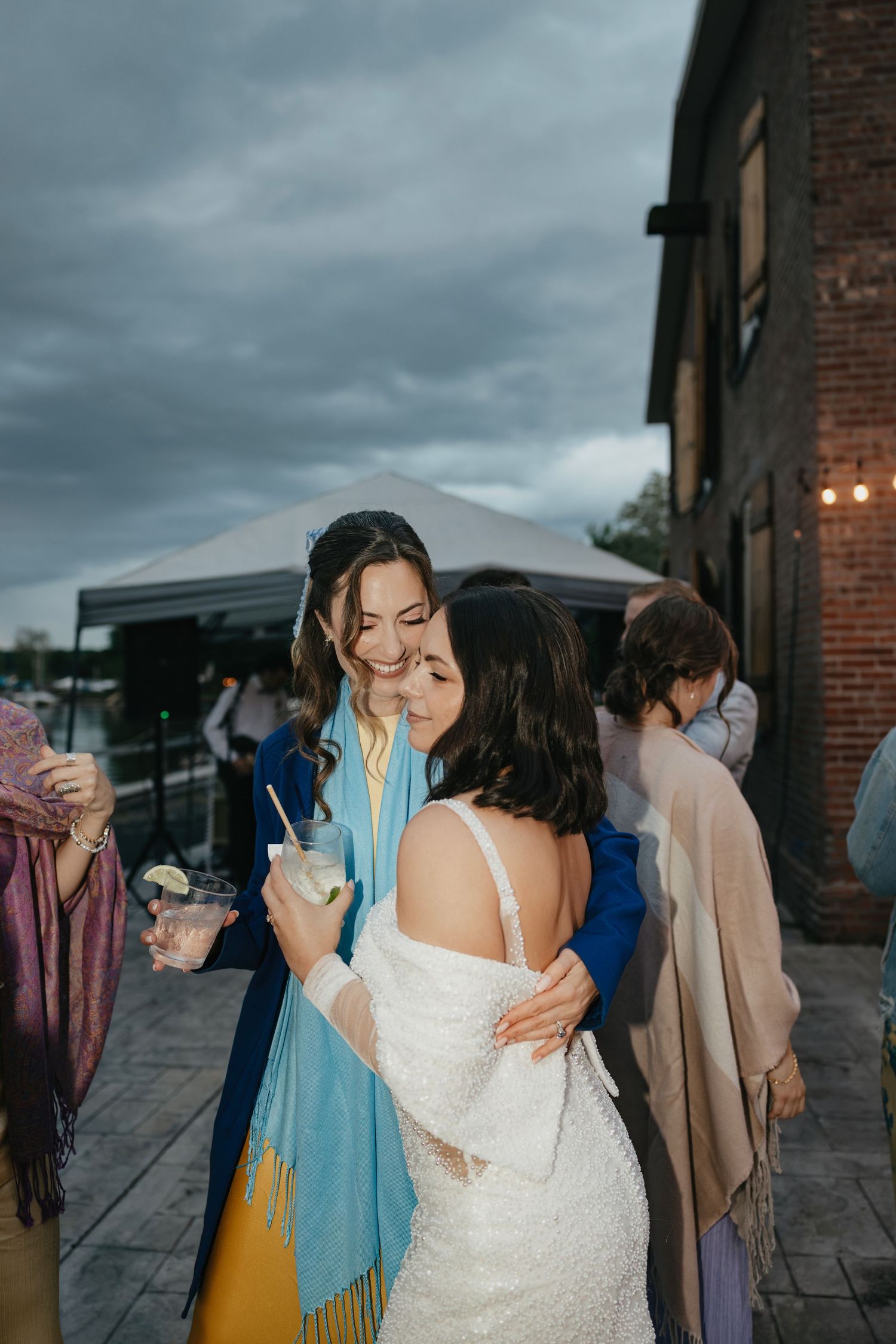 A sequence of emotional moments at a wedding showing embraces between guests against a brick building backdrop.