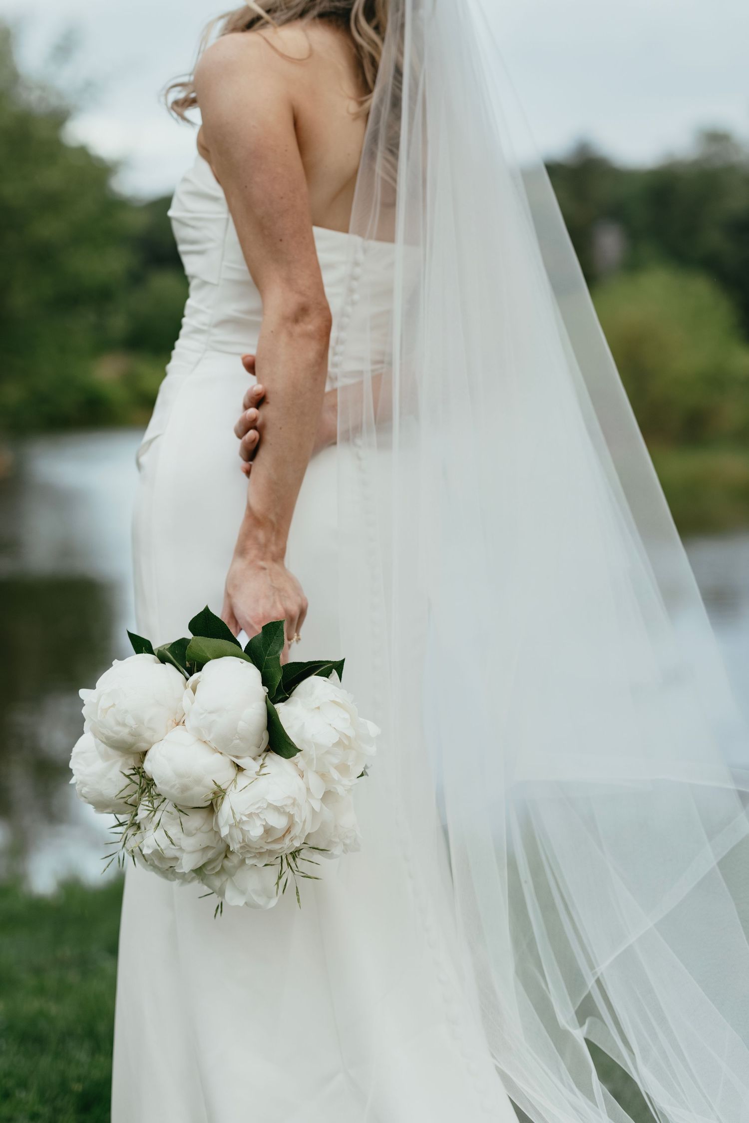 Close-up details of a bride's flowing white veil and elegant white rose bouquet in an outdoor garden setting.