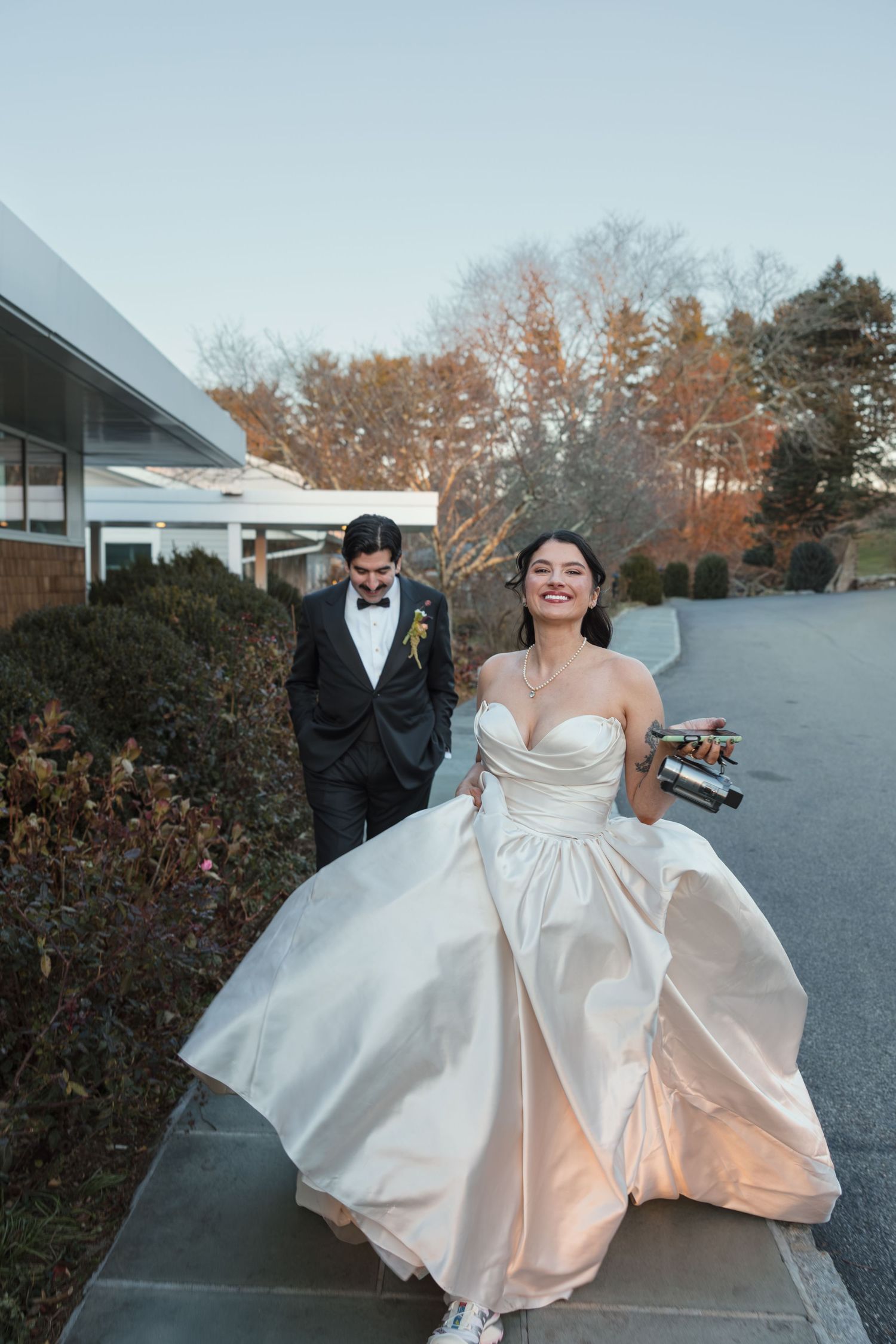 A joyful wedding couple runs playfully through an outdoor venue with the bride's white dress flowing in the wind.