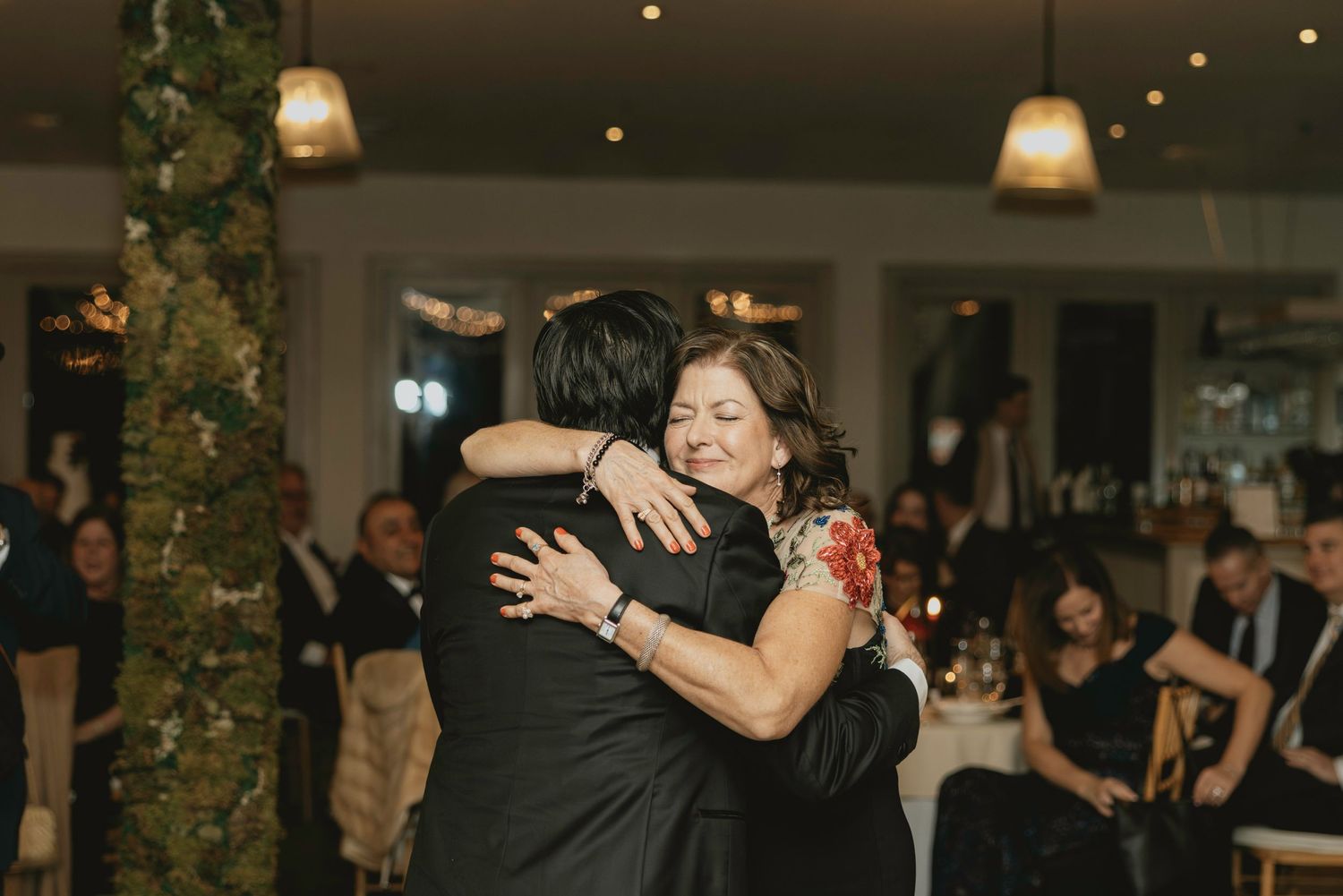 Wedding guests dance and celebrate together at an indoor reception with hanging pendant lights and festive decor.