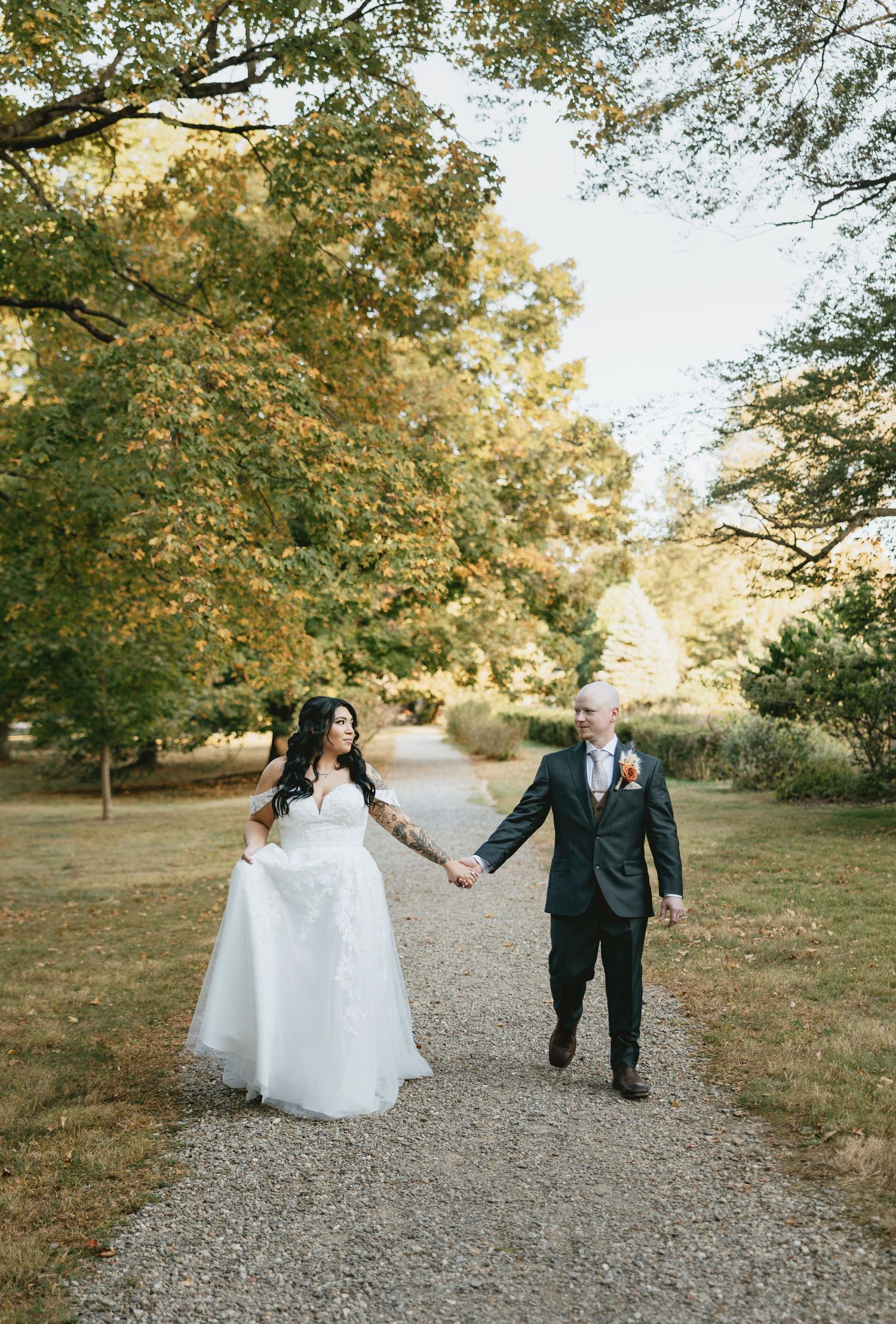 A couple walks together on a gravel path surrounded by autumn trees with golden leaves in a park setting.