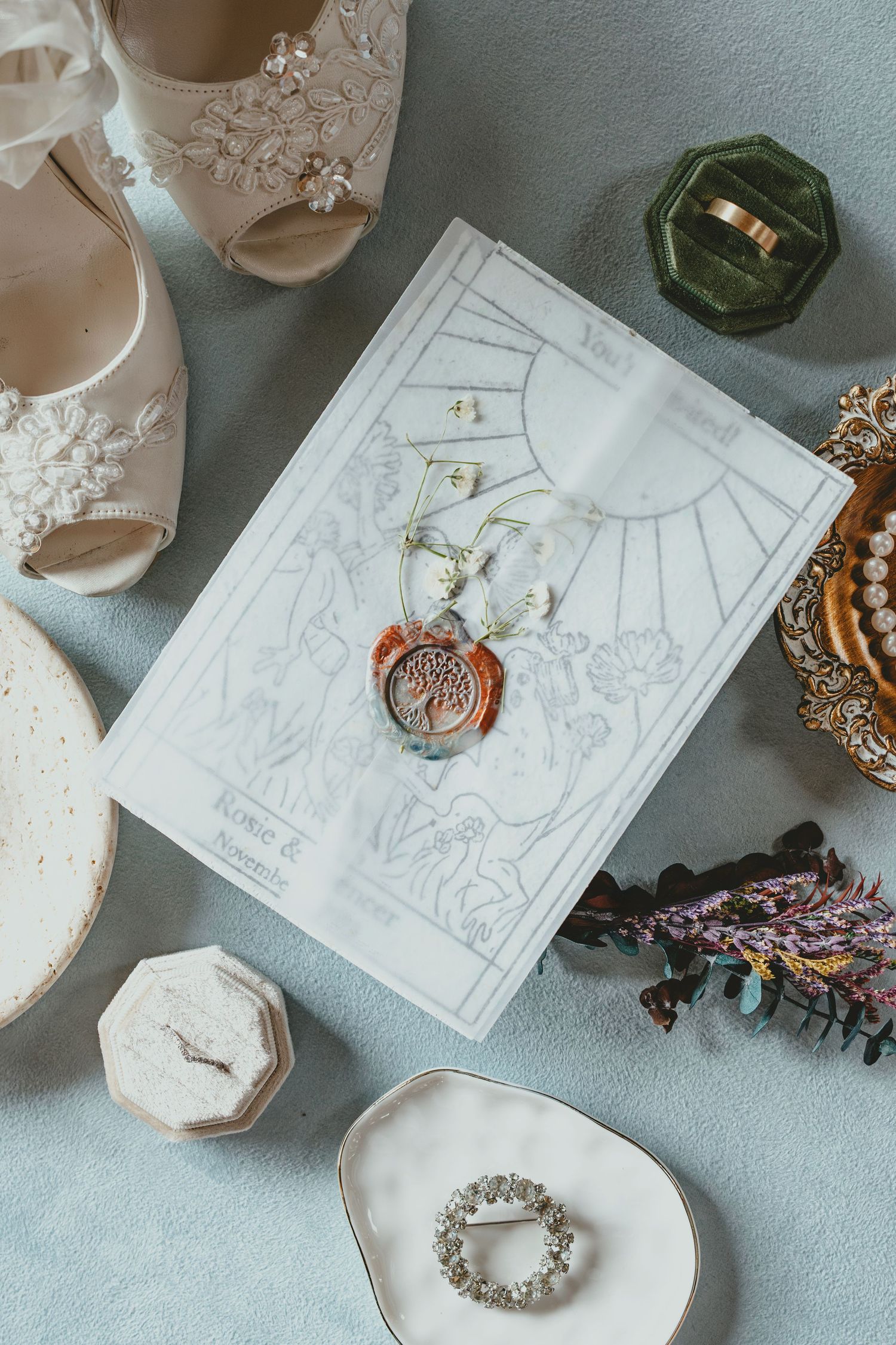 Wedding accessories including jewelry, invitations, and delicate white shoes arranged on a light blue surface.