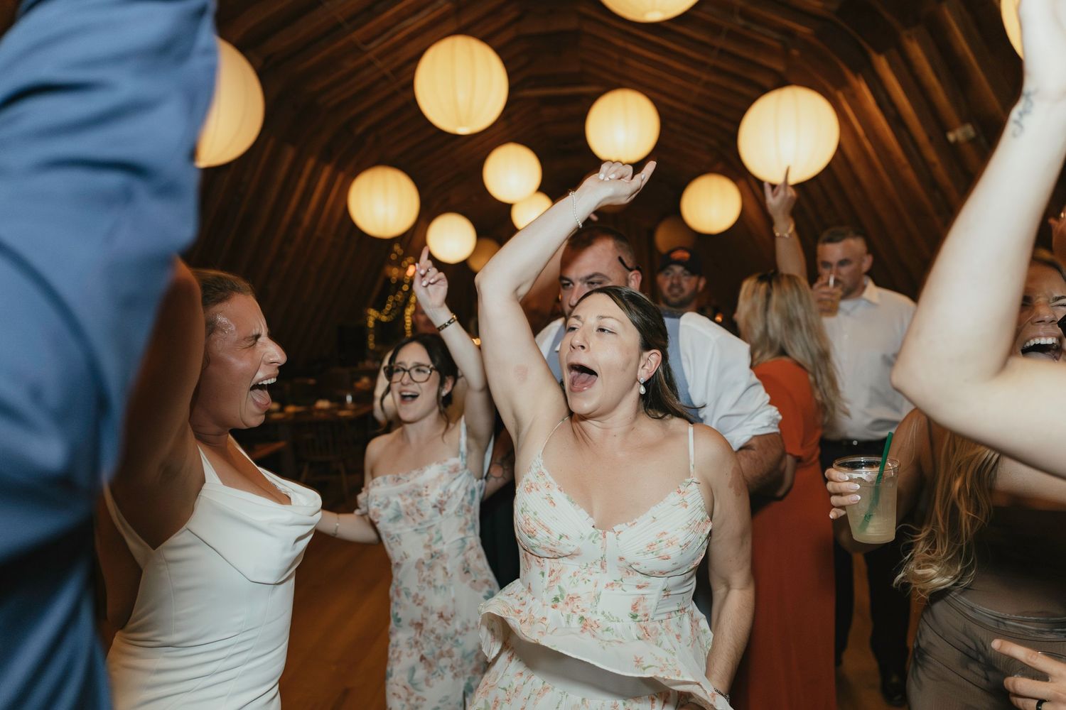 Joyful dancing and celebration taking place at a wedding reception under warm lighting and wooden beams.